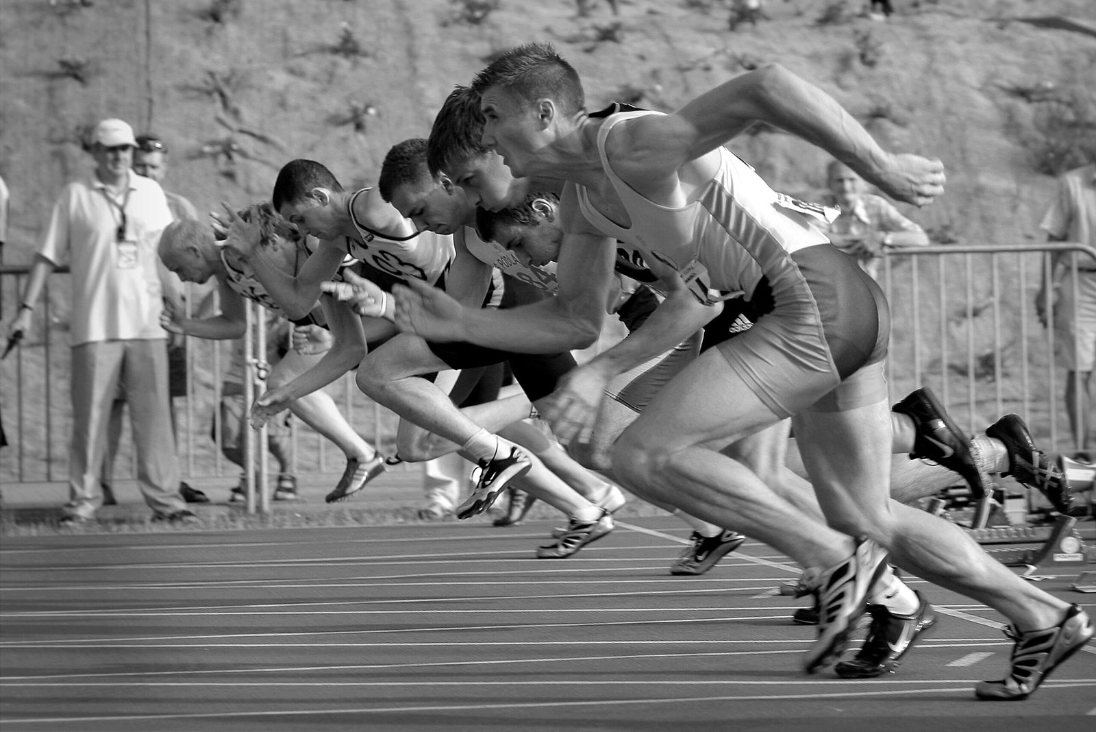 Athletes burst from the blocks during a sprint race, captured in monochrome.